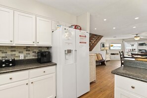 A kitchen with white cabinets, a refrigerator, a coffee maker, and a staircase leading to a balcony. - Dog-Friendly 3BR · Gulf Beach Steps Away· Sleeps 9 (Port St. Joe)