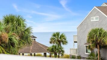 A beachfront property with a gazebo, a small building, and a house with a balcony overlooking the sea.