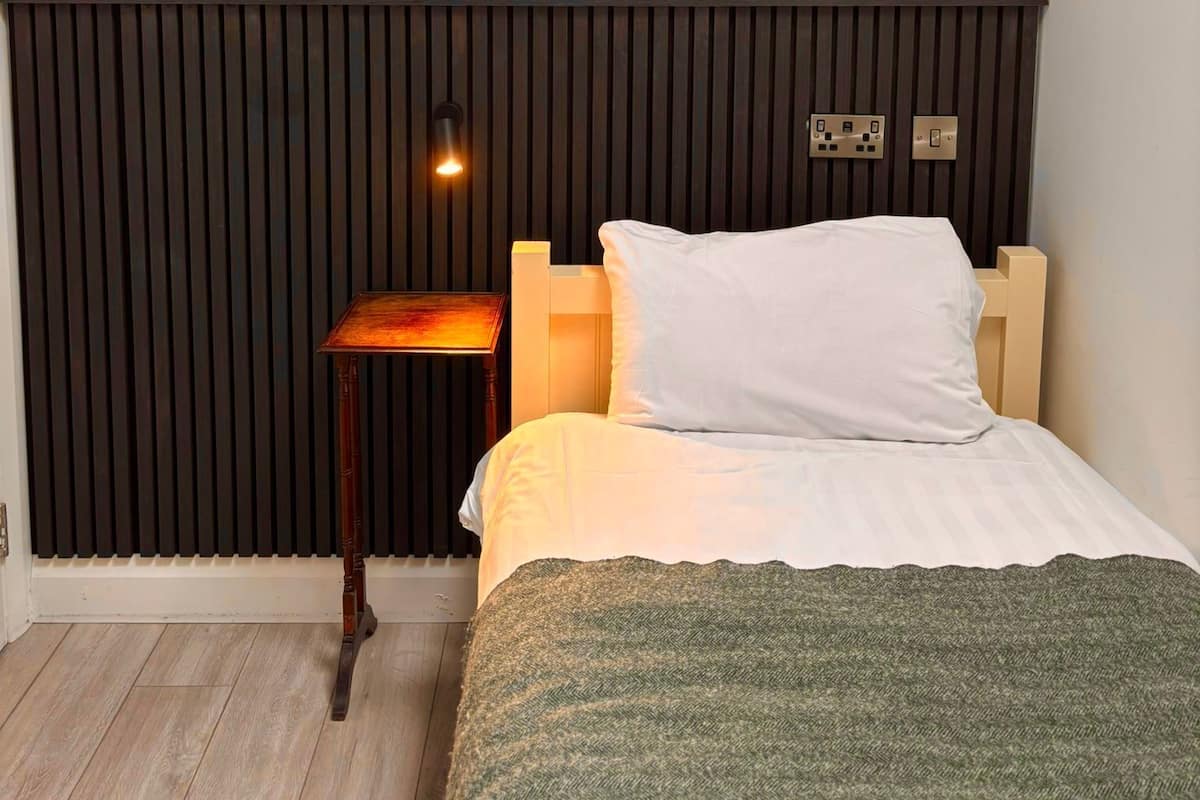 A bedroom with a bed, a bedside table, and a wall-mounted light fixture.