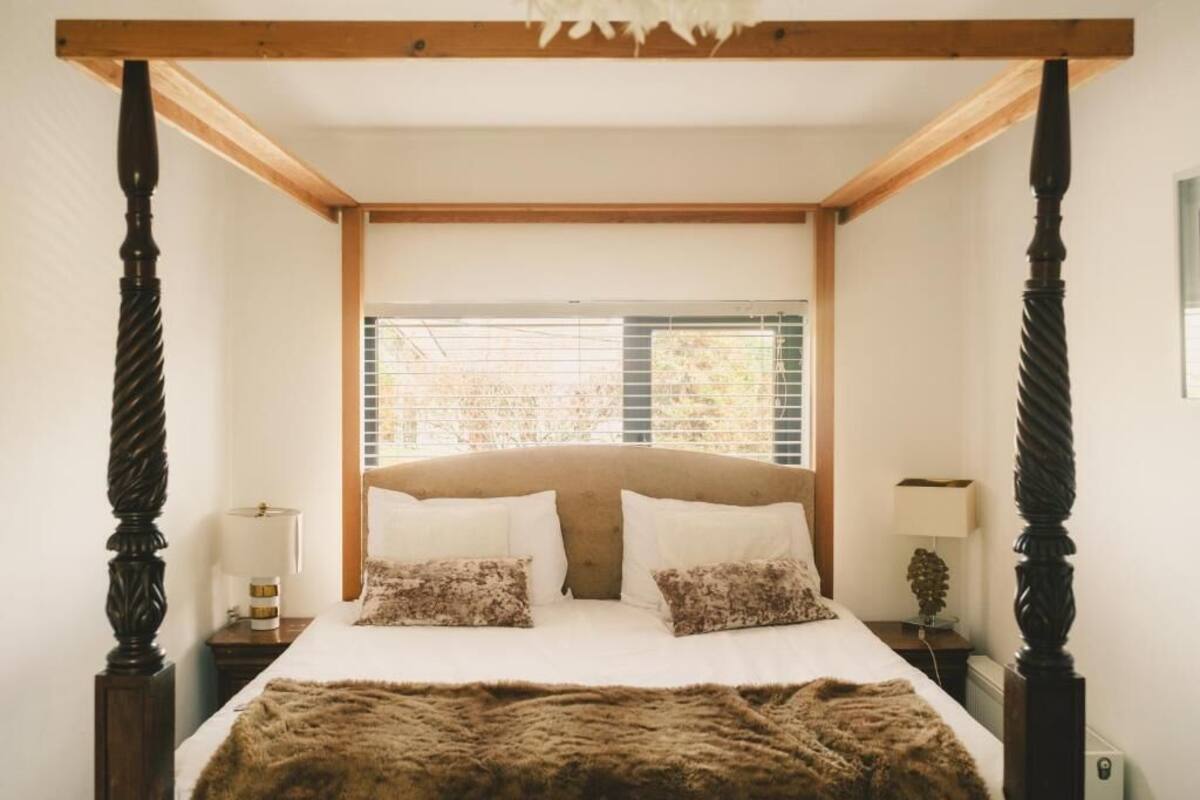 A bedroom with a four-poster bed, wooden headboard, and a window with blinds.