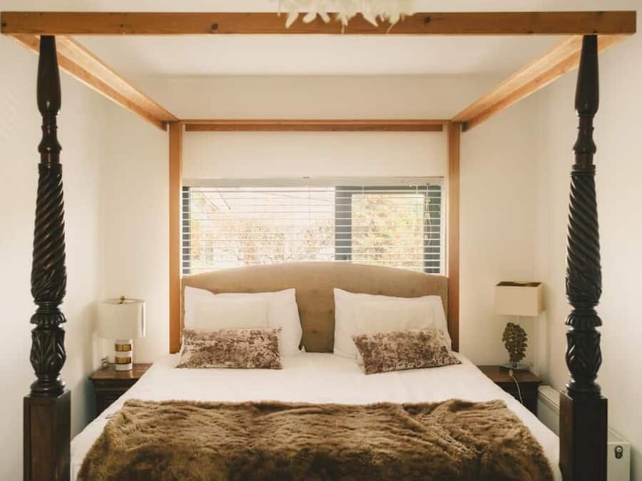 Un dormitorio con cama con dosel, cabecero de madera y ventana con persianas.