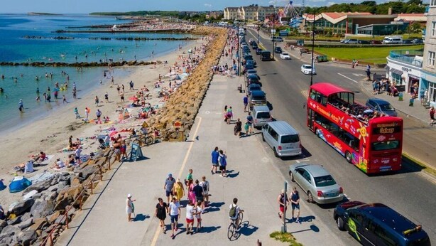 A coastal road with a beach on one side, a Ferris wheel, and a red double-decker bus. - 1997 Stays Galway (Galway)