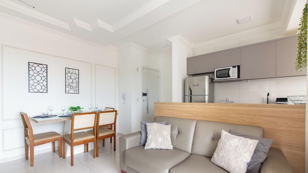 A modern living room with a sofa, dining table, chairs, and a kitchen area with cabinets and appliances. - Modern apt w/ Barbecue 600m From the Beach Com305 (Florianópolis)