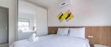 Habitación de hotel moderna con una cama grande, una mesita pequeña y un equipo de aire acondicionado en la pared.