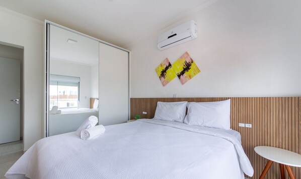 Habitación de hotel moderna con una cama grande, una mesita pequeña y un equipo de aire acondicionado en la pared.