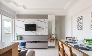 Un espace repas moderne avec une table en verre, des sets de table bleus et un téléviseur fixé sur un mur en marbre.