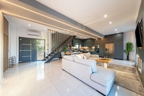 Un salon moderne avec un escalier, une cuisine et un téléviseur à écran plat.