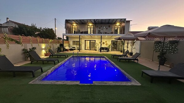 Une maison à deux étages avec une piscine, un espace salon extérieur et des plantes en pot.