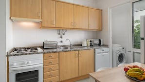 A modern kitchen with wooden cabinets, a gas stove, a microwave, a toaster, and a washing machine. - Close to all facilities | Madalena Living Apt (Funchal)