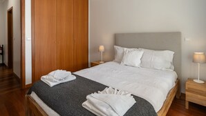 A neatly made bed with white linens, two bedside lamps, and a wooden wardrobe. - Close to all facilities | Madalena Living Apt (Funchal)