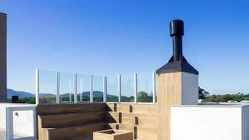 Una terraza en la azotea con chimenea, barandillas de vidrio y mobiliario de madera.