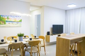 Uma zona de refeições moderna com uma mesa posta para quatro pessoas, uma televisão sobre um móvel e um quadro na parede.