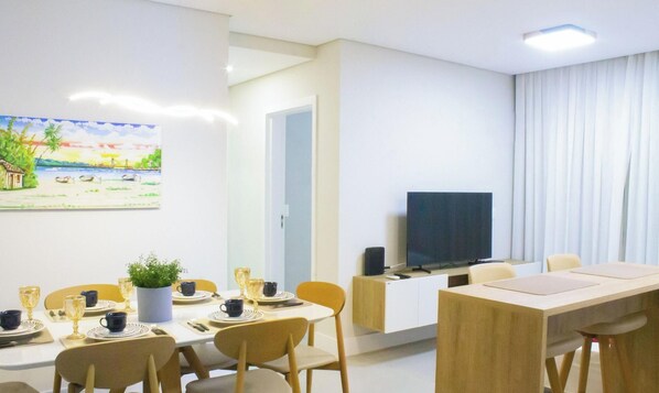 A modern dining area with a table set for four, a television on a stand, and a painting on the wall.