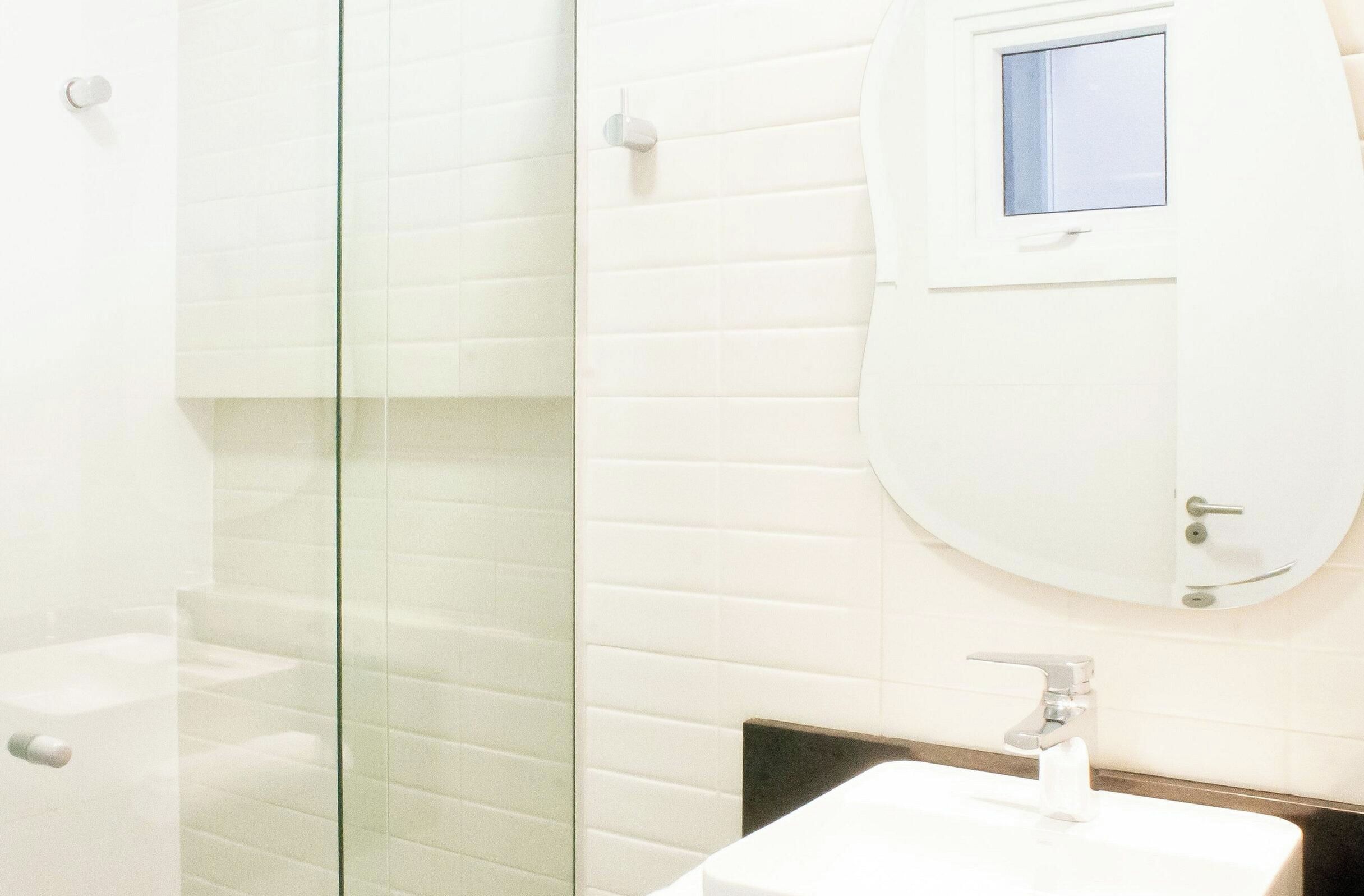 Un baño con cabina de ducha de vidrio, un lavabo blanco y un espejo con un pequeño ventanal.