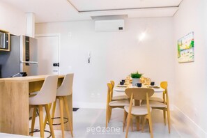 Uma cozinha moderna com micro-ondas e frigorífico integrados, um espaço de refeições com mesa redonda e cadeiras, e um quadro na parede.