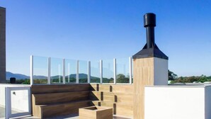 Eine Dachterrasse mit Schornstein, Glasabdeckung und Holzmöbeln.