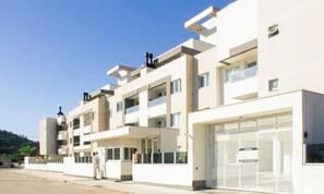 Un moderno edificio residencial de varios pisos con balcones, entrada con portón y cielo despejado.