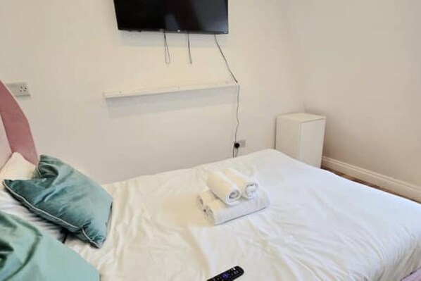 A hotel room with a bed, a TV mounted on the wall, and a small white shelf.