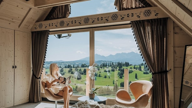 Een gezellige kamer met een groot raam, houten wanden en uitzicht op een groen landschap met bergen.