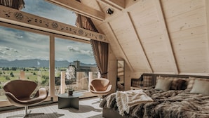 Een slaapkamer met een groot raam, een bed, twee stoelen en een kleine tafel.
