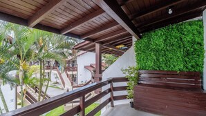 Un espacio exterior techado con barandillas de madera, una escalera y una pared verde de plantas artificiales.
