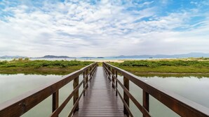 Un puente de madera que lleva a una playa con aguas tranquilas y montañas a lo lejos.