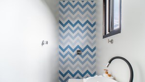 Un baño con una pared estampada en patrón de espiga, una ventana, un lavabo y un grifo.