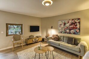 A living room with a sofa, a TV, a floral painting, a wooden cabinet, and a window. - Casa 'Gall' with Mountain Views, Wi-Fi, and Air Conditioning (Espolla)