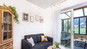 Ein Wohnzimmer mit einem dunkelblauen Sofa, einem Holzschrank, einer Glastür, die zu einer Terrasse führt, und gerahmten Bildern an der Wand.