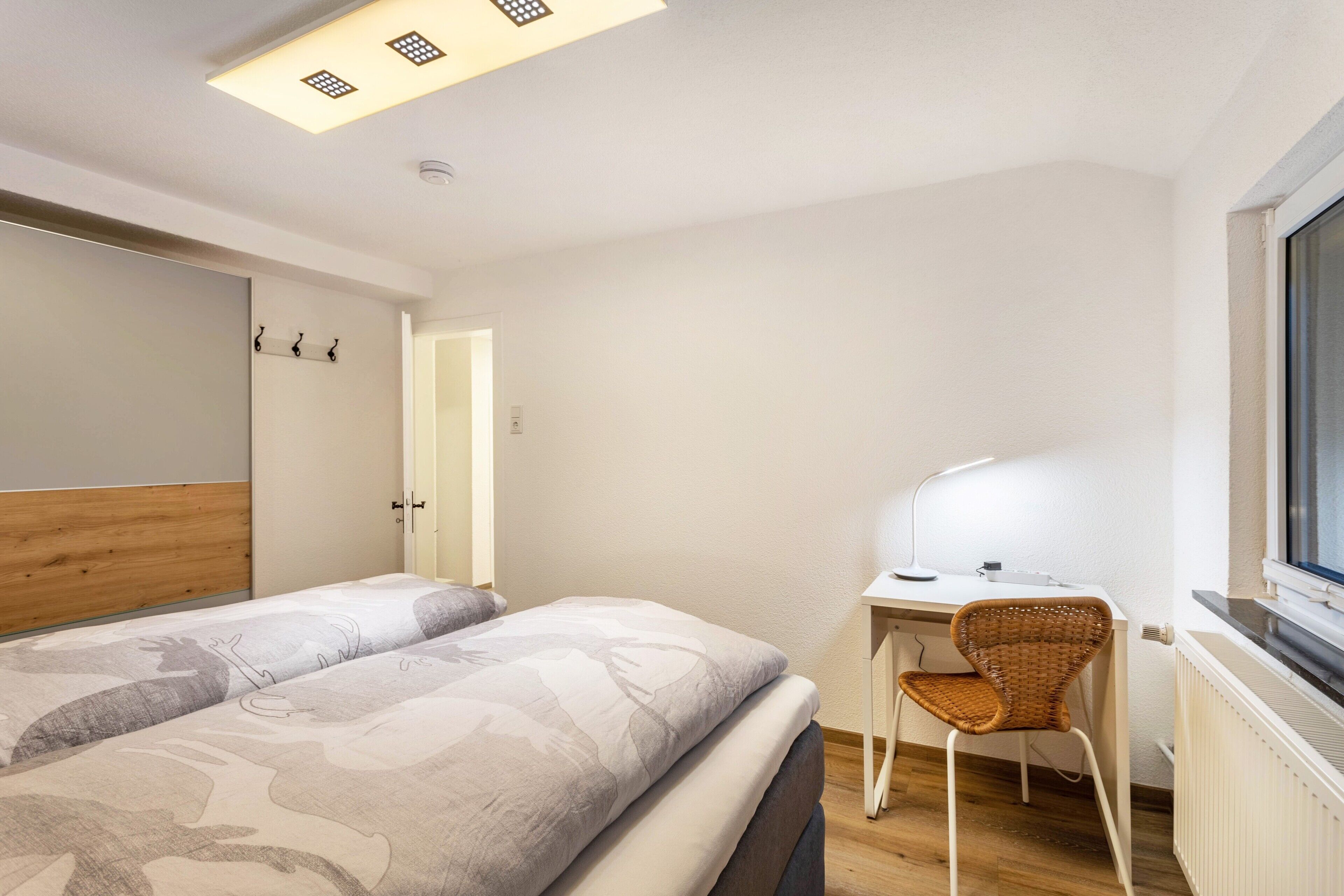 A bedroom with a bed, a desk, a chair, and a window.