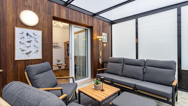 Ein modernes Interieur mit einer Holzwand, einer Couch, Sesseln, einem Tisch und einer gerahmten Vogelillustration.