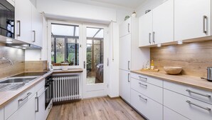 Eine moderne Küche mit weißen Schränken, einer Holzarbeitsplatte, einem eingebauten Ofen und Blick durch eine Glastür in einen Außenbereich.