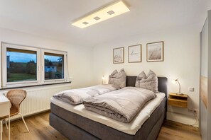Un dormitorio con cama, escritorio, silla, mesita de noche y ventana con vistas.