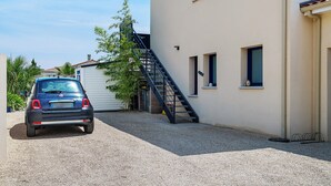 Un coche estacionado en una entrada, un edificio con escaleras y un cielo despejado.