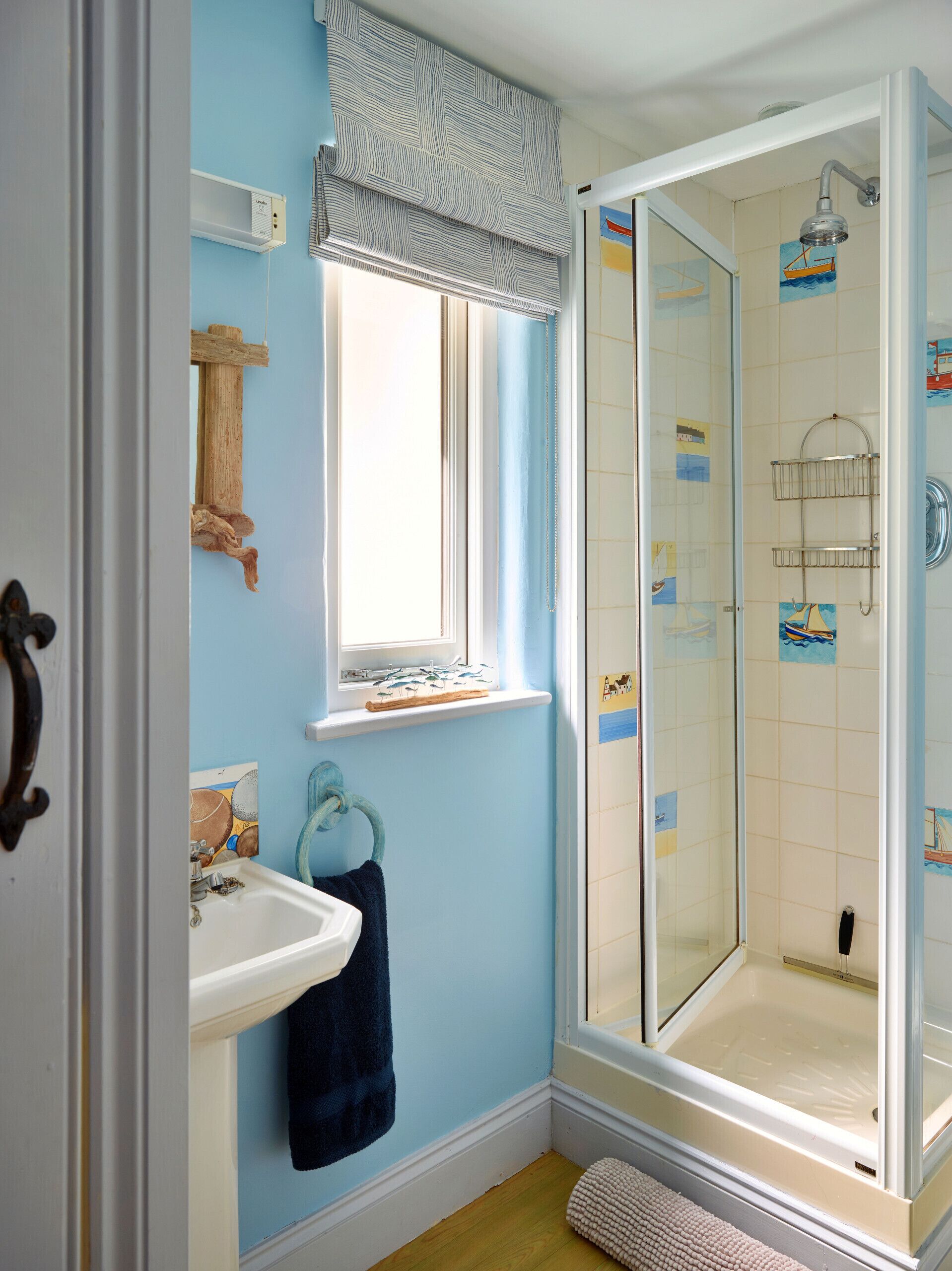 A bathroom with a shower, a sink, a window with a striped valance, and a towel rack.