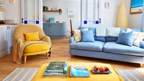 A living room with a yellow armchair, a blue sofa, and a coffee table with books and apples.