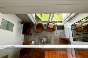 Un intérieur moderne avec un plafond en verre, deux fauteuils marron ornés de coussins, une petite table ronde et un plancher en bois.