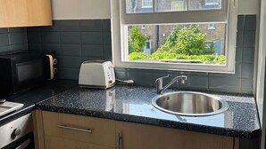 A kitchen with a black countertop, stainless steel sink, and a window with a view of buildings and greenery.