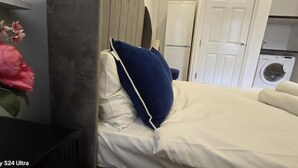 A bed with white and blue bedding, a white door, and a washing machine in the background.
