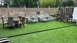 A backyard with a lawn, a wooden deck, and outdoor furniture including chairs and a table.