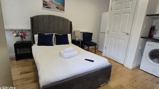 A hotel room with a bed, a nightstand, a chair, a washing machine, and a door.