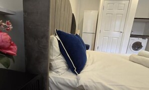 A bed with white and blue bedding, a white door, and a washing machine in the background.