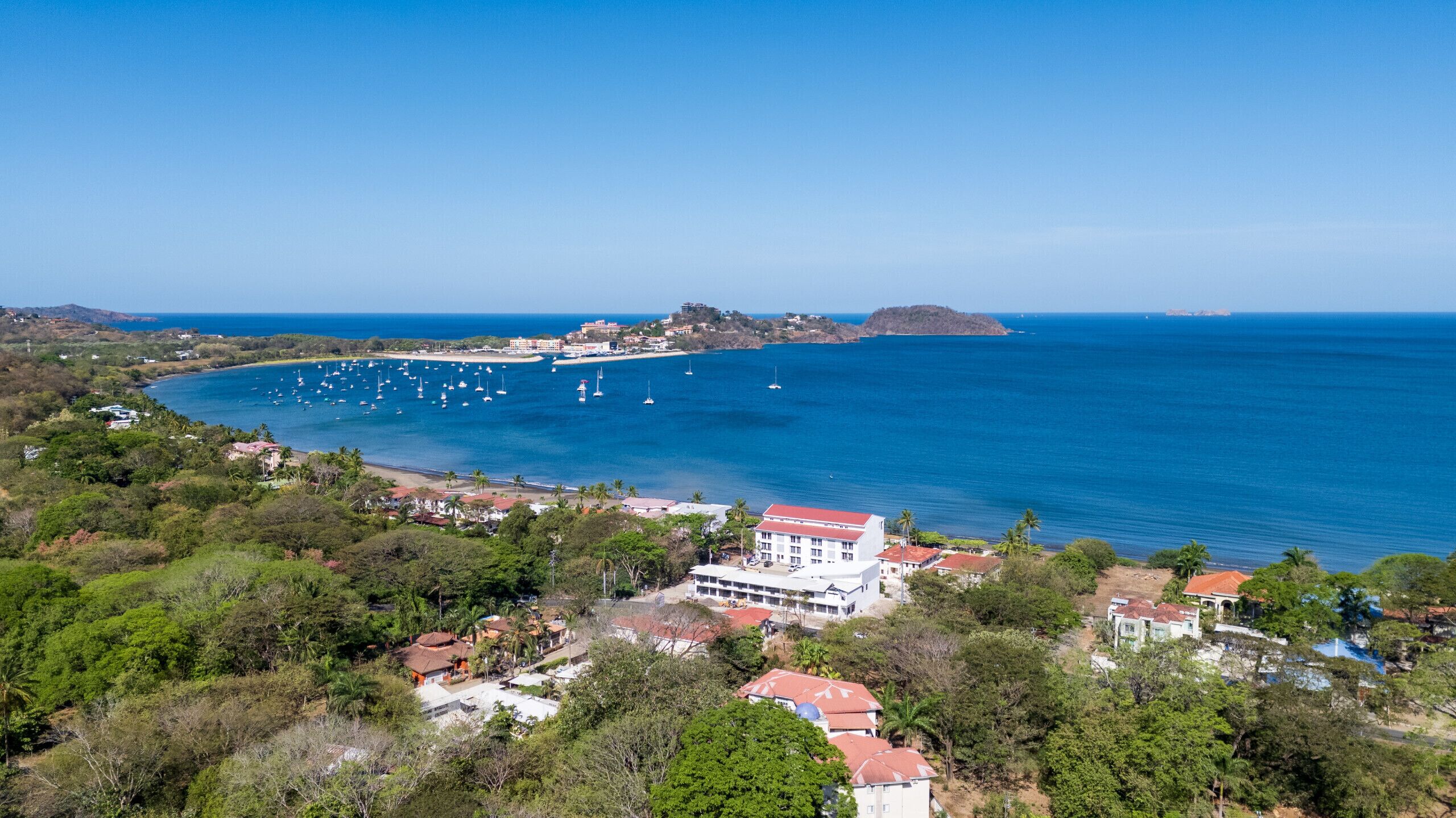 A coastal area with a large body of water, several boats, and a prominent building with a red roof.