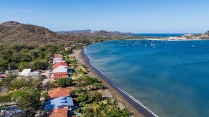 An aerial view of a coastal area with a beach, houses with red roofs, and a clear blue sea with boats. - Beachfront Condo In Costa Rica (Tempate)
