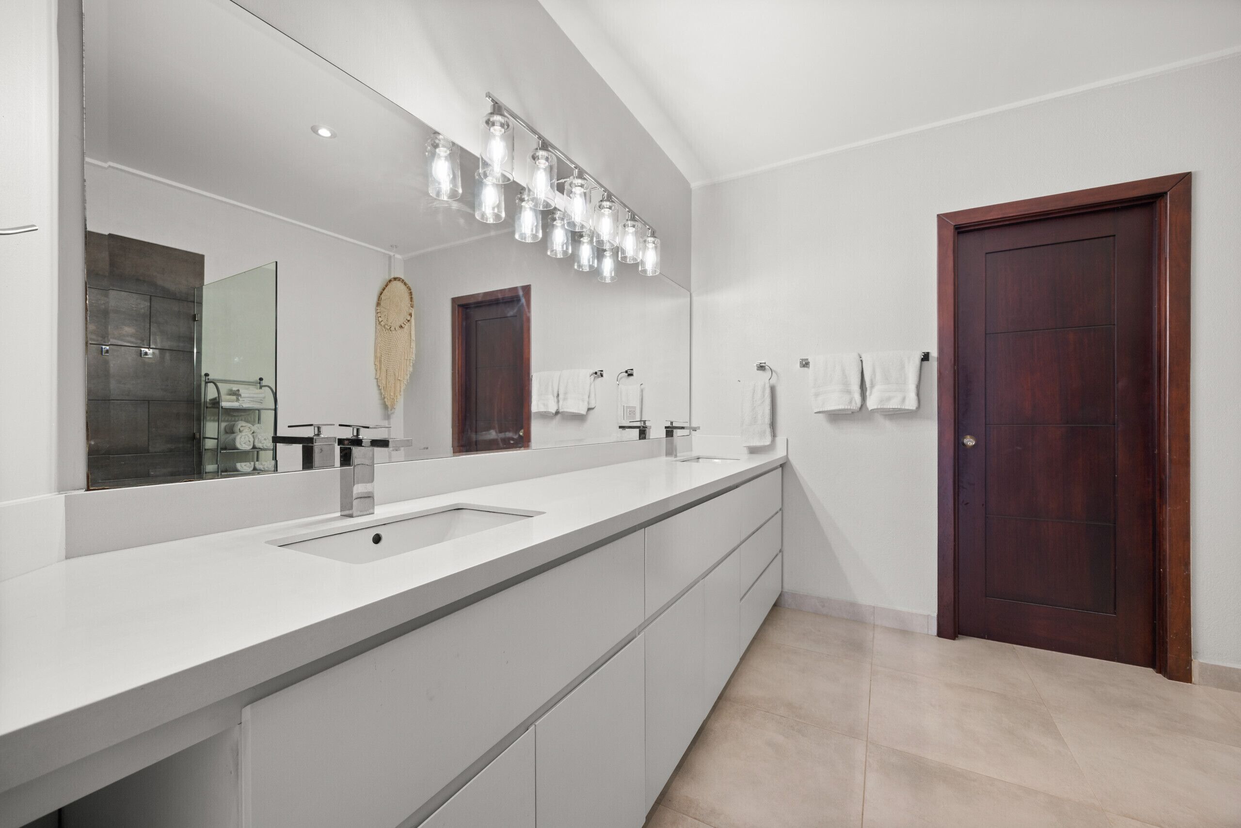 A modern bathroom with a large mirror, two sinks, and a wooden door.
