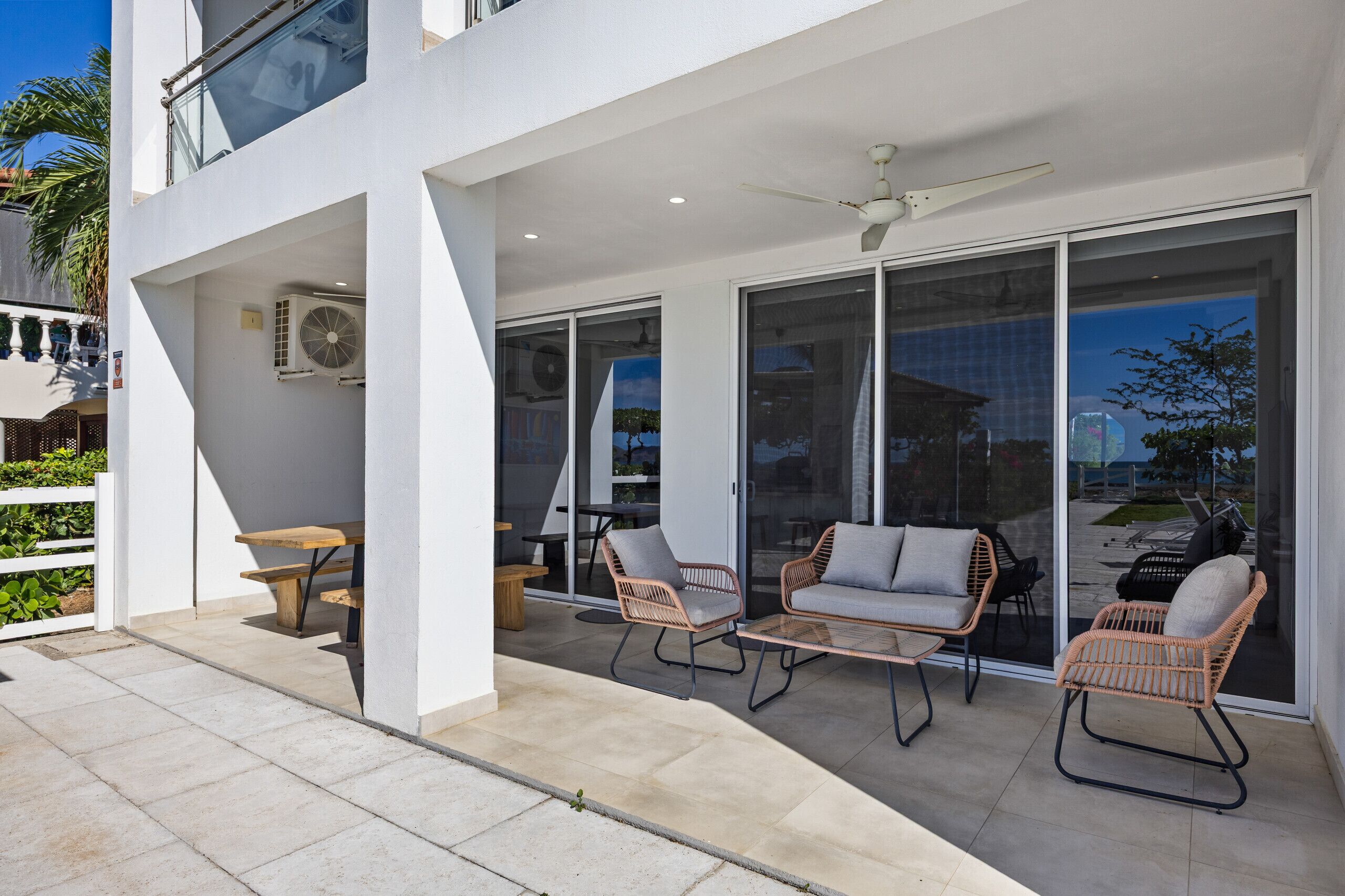 A modern outdoor patio with wicker furniture, a ceiling fan, and large sliding glass doors.