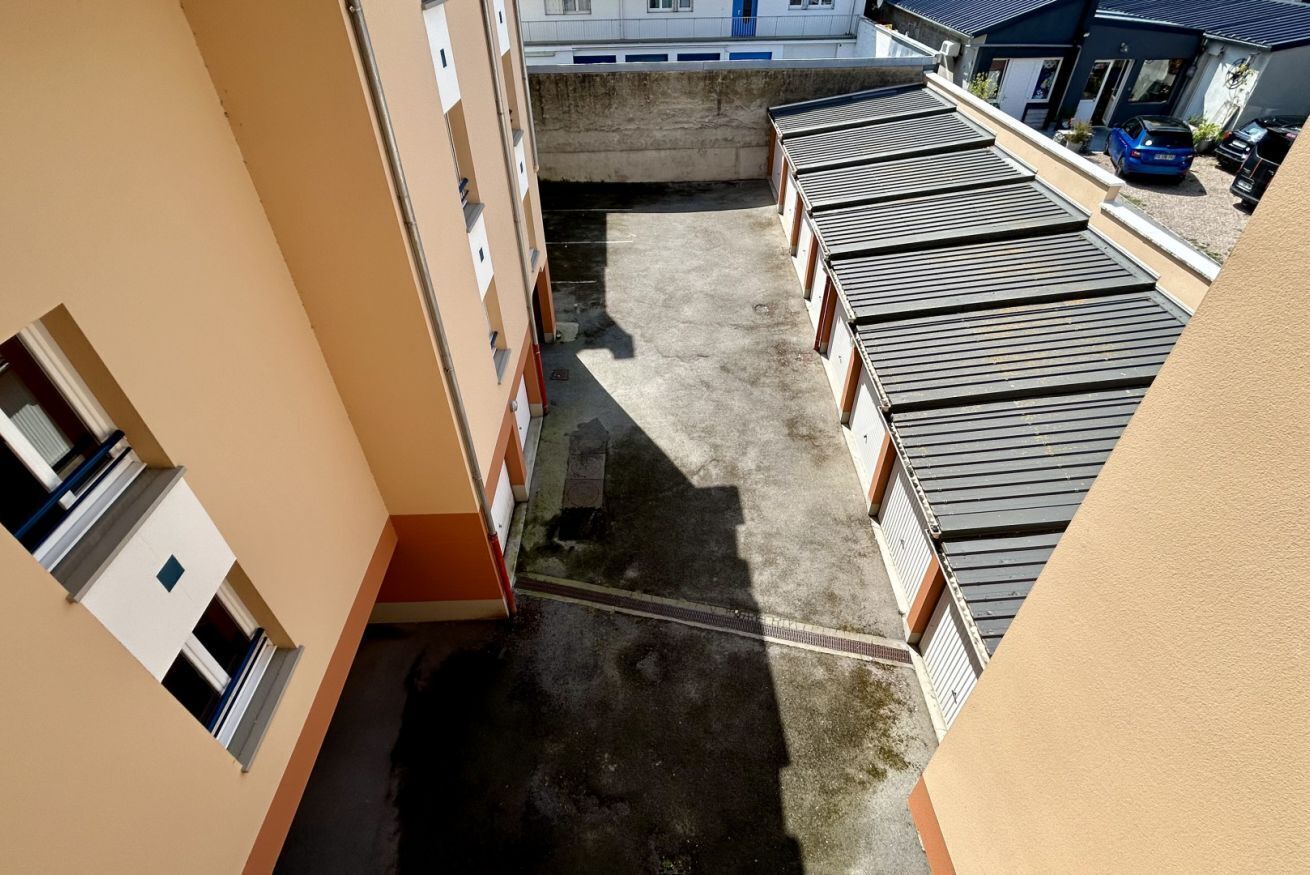 Un immeuble à plusieurs étages doté d’une cour intérieure, de balcons et d’une voiture bleue garée à l’extérieur.