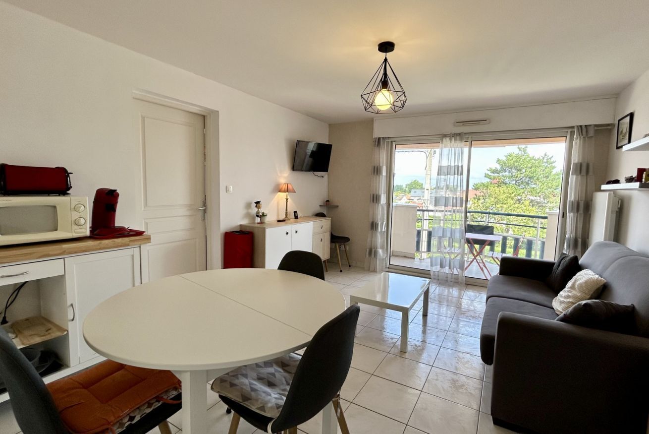A modern living room with a dining area, a sofa, a TV, and a balcony with a view.