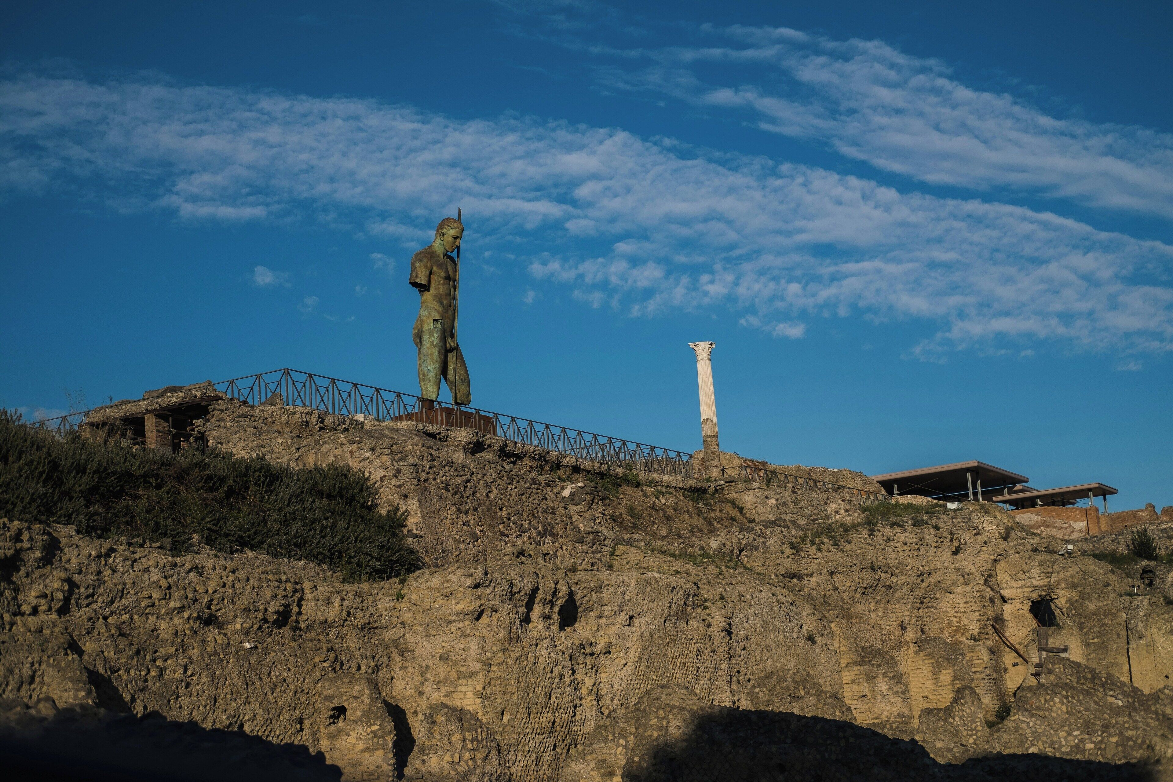 A statue on a rocky hill with a modern building in the background.