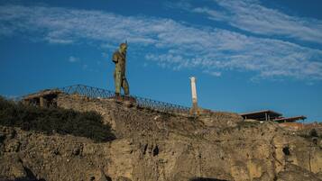 A statue on a rocky hill with a modern building in the background.